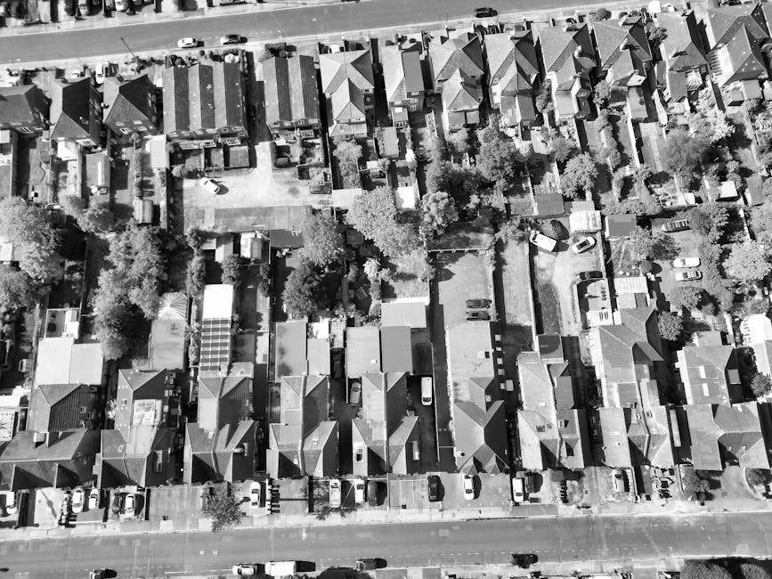 An aerial black-and-white photograph of a residential neighbourhood showing a variety of garden spaces, lawns, and paved pathways. The gardens are enclosed by fences or hedges, with some featuring mat